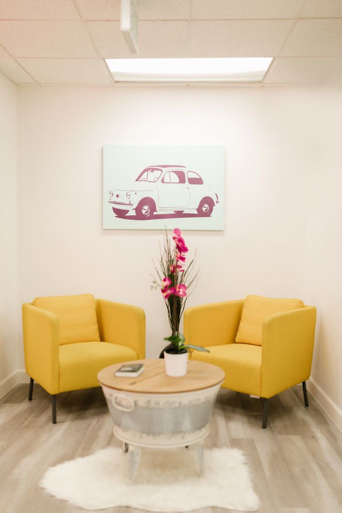 Bright waiting area featuring yellow chairs, a modern table, and car artwork.